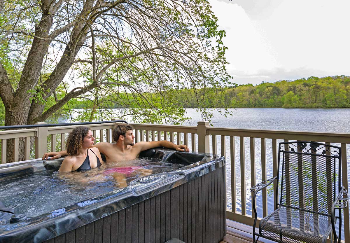 young couple in hot tub overlooking lake at lakeside camp cabins