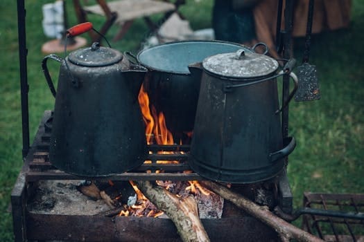 Camp kettles and pot over open fire at an outdoor campsite, ideal for rustic cooking themes.